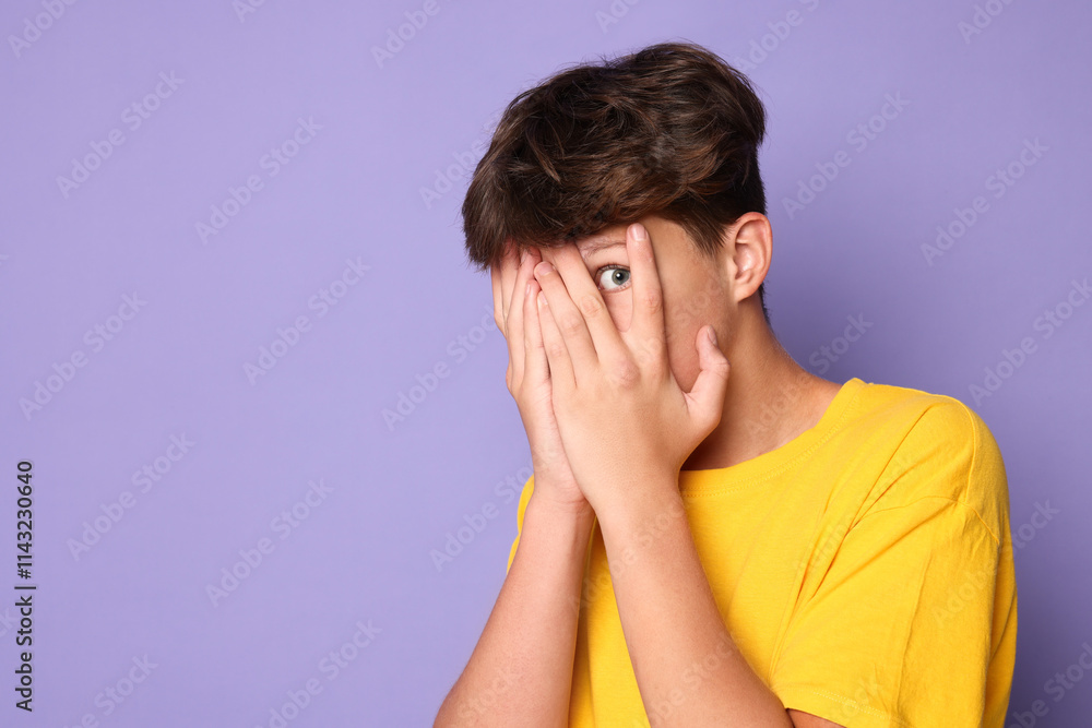 Scared teenage boy covering face with hands on violet background. Space for text Scared teenage boy covering face with hands on violet background. Space for text