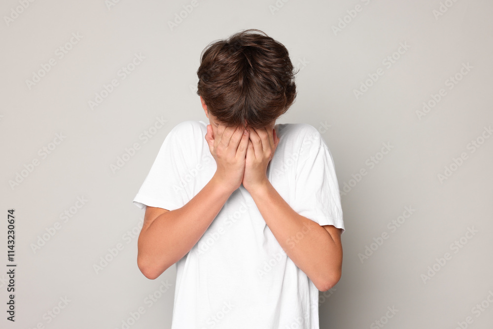 Scared teenage boy covering face with hands on grey background Scared teenage boy covering face with hands on grey background