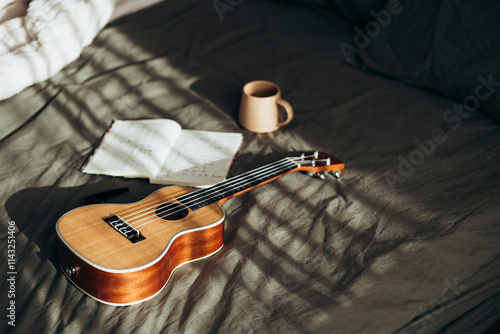 Ukulele and open notebook on sunlit bed with cozy mug scene photo