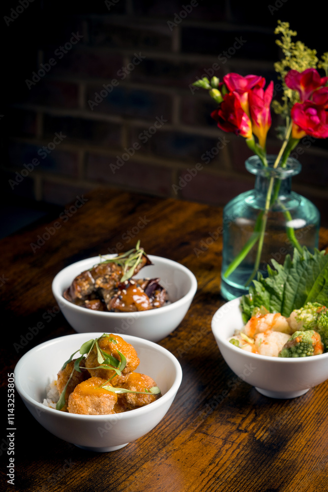 Three bowls of assorted Asian dishes with flower vase on table Three bowls of assorted Asian dishes with flower vase on table