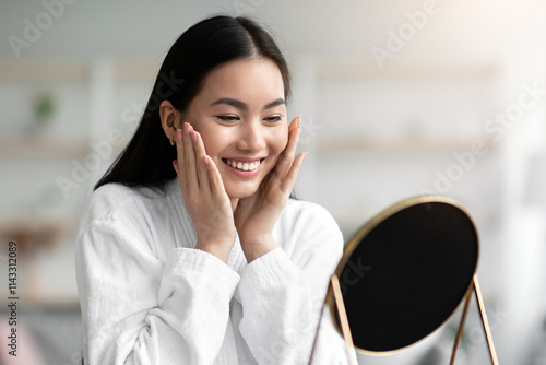 Cuadro en lienzo Pretty asian woman in bathrobe making face-lifting massage, sitting at table in