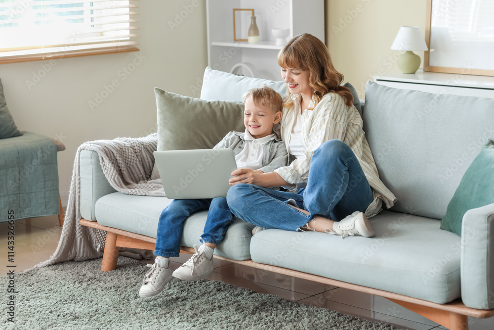 Happy mother and her little son with laptop sitting on sofa in living room at home Happy mother and her little son with laptop sitting on sofa in living room at home