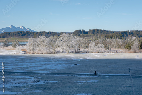 Frozen nature of the Alps on a winter morning. Frozen trees covered in frost. A lone cyclist rides along a dirt road through a frozen field photo