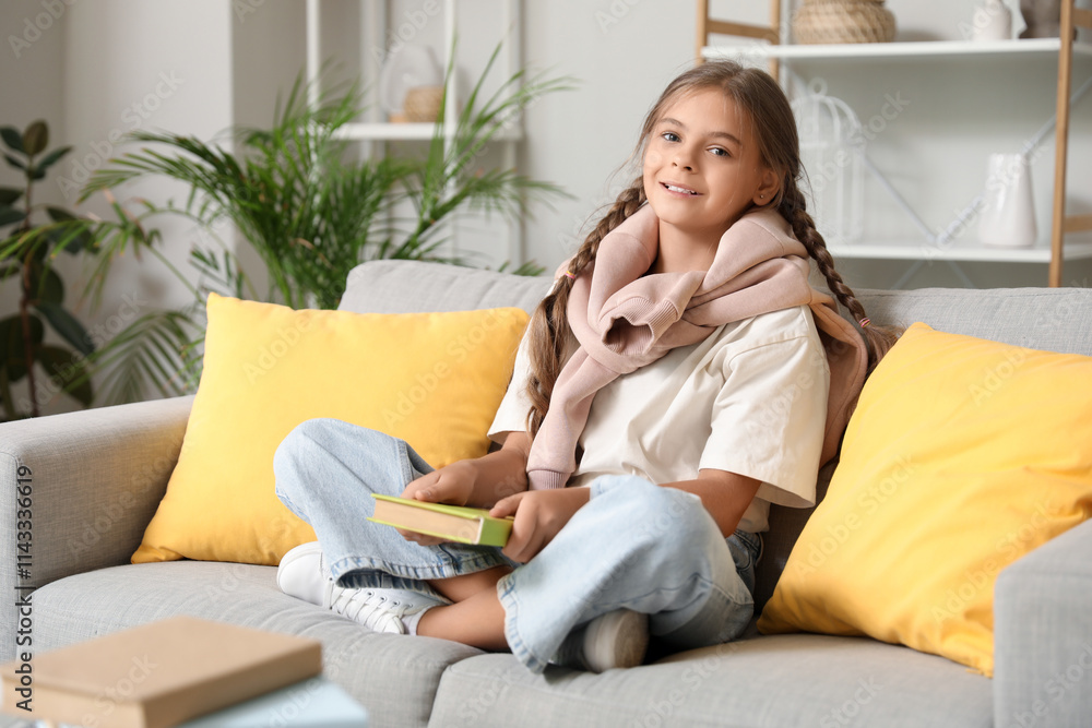 Cute schoolgirl with book sitting on sofa in living room Cute schoolgirl with book sitting on sofa in living room