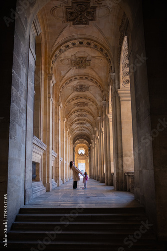 A young mother and her daughter are walking through an old building in Paris. A columned gallery with high patterned ceilings and a mother and daughter enjoying a walk photo