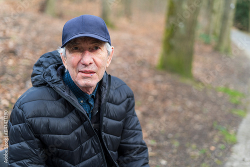 An elderly man in a jacket and hat sits alone on a bench in a park. The concept of loneliness in old age