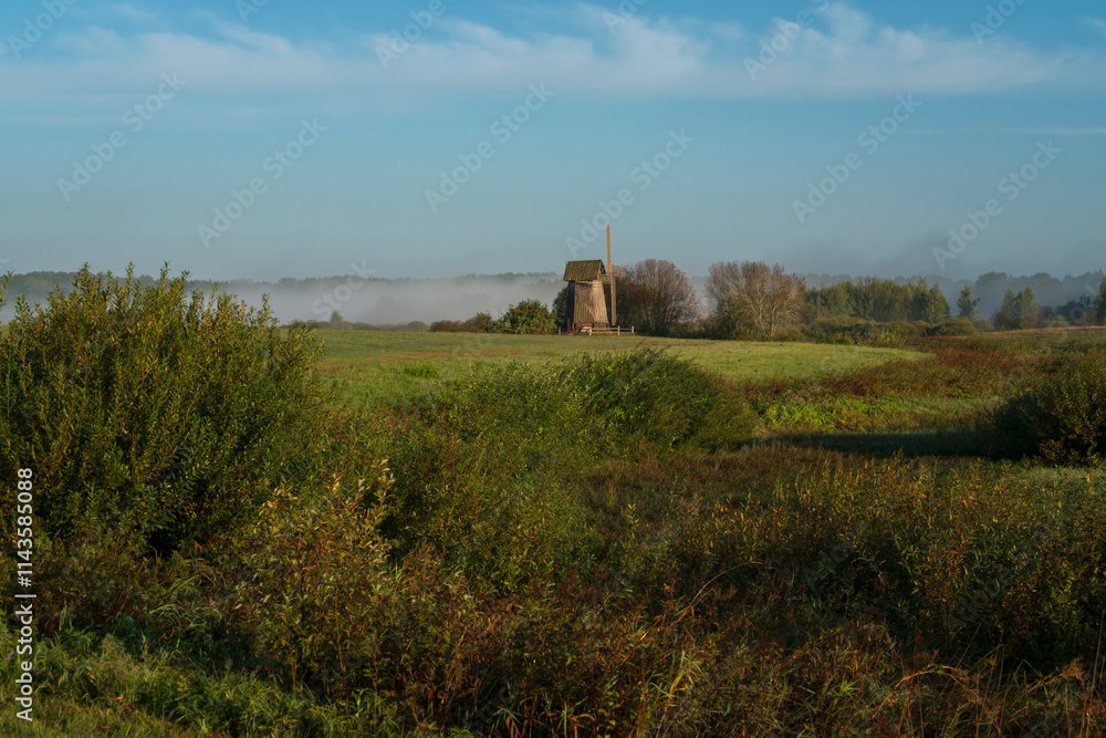 View of an ancient wooden windmill on the banks of the Sorot River on a foggy summer morning, Mikhailovskoye, Pushkinskiye Gory, Pskov region, Russia View of an ancient wooden windmill on the banks of the Sorot River on a foggy summer morning, Mikhailovskoye, Pushkinskiye Gory, Pskov region, Russia