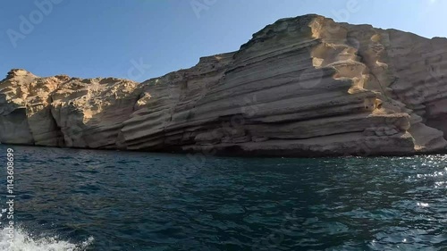 A magnificent rock formation juts out of the tranquil waters waves passing, revealing layered textures and captivating shapes that tell the story of time at Mina Al Fahal in Muscat, Oman.