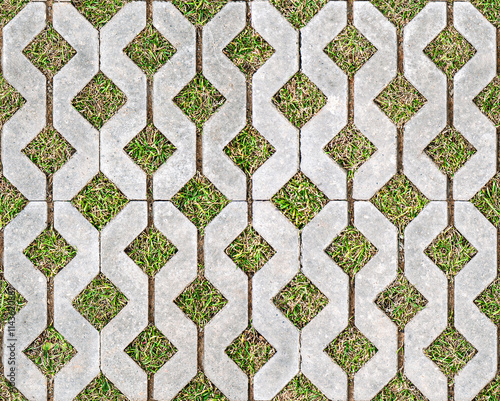 Geometric concrete paving stones with grass-filled gaps, arranged in a repetitive pattern on a flat surface. Seamless texture