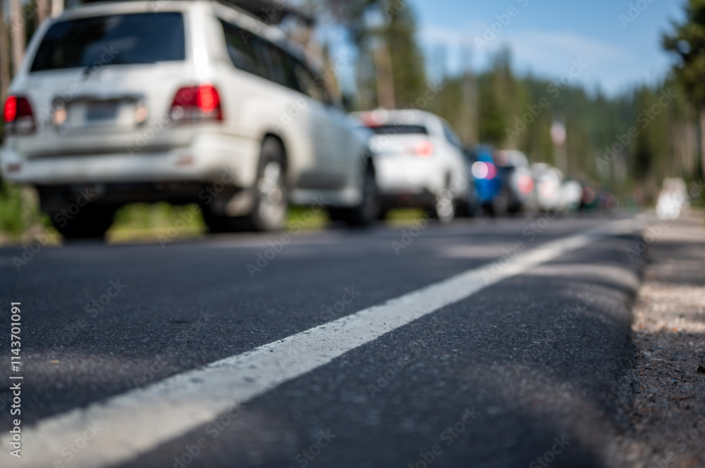 Selective focus on a paved road with a defocused long line of vehicles to enter a national park in the background Selective focus on a paved road with a defocused long line of vehicles to enter a national park in the background