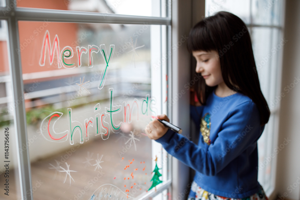 Cute little girl drawing merry christmas wishes on window Cute little girl drawing merry christmas wishes on window