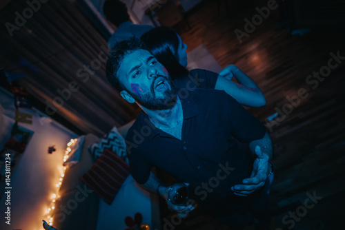 A man with face paint is having a lively time at a birthday party. The dim lighting and festive atmosphere set the scene for celebration and enjoyment. photo