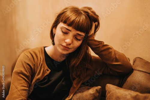 A thoughtful woman sits alone in a warm, cozy coffee shop, resting her head in contemplation. The subdued lighting and gentle ambiance suggest a moment of reflection and introspection. photo