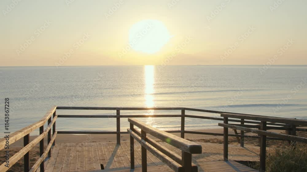 Old wooden bridge leading to the beach, the sea at sunset and the glare of the sun on the water Old wooden bridge leading to the beach, the sea at sunset and the glare of the sun on the water