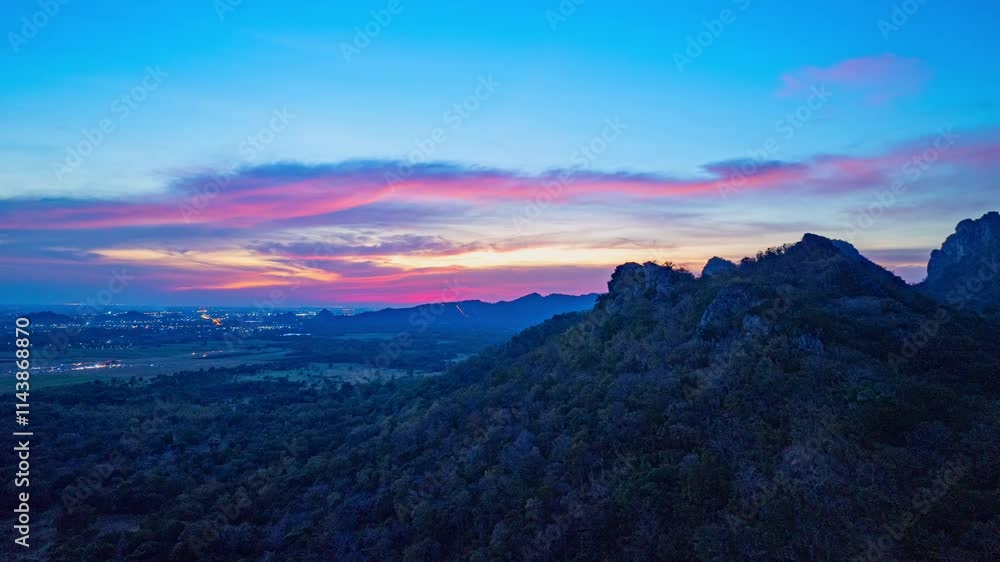 A panoramic view of dramatic mountain peaks silhouetted against a vibrant sunset sky, with fiery hues of red, orange, and pink blending into the fading blue. sunflowers fields around the mountains.