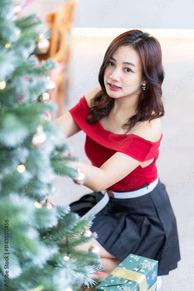 Portrait of beautiful happy Smiling asian woman relaxing In a red dress decorating to a Christmas tree at home in the living room indoors Decoration During Christmas x-mas and New Year holidays. Portrait of beautiful happy Smiling asian woman relaxing In a red dress decorating to a Christmas tree at home in the living room indoors Decoration During Christmas x-mas and New Year holidays.