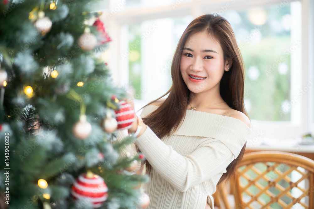 Portrait of beautiful happy Smiling asian woman relaxing sitting decorating to a Christmas tree at home in the living room indoors Decoration During Christmas x-mas and New Year holidays.