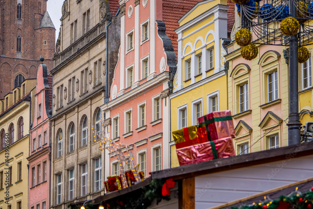 Fototapeta premium stalls at a Christmas and New Year's market in a big city. Christmas tree decorations and decorations, lights, baubles, garlands against the background of urban architecture, old historic tenement hou