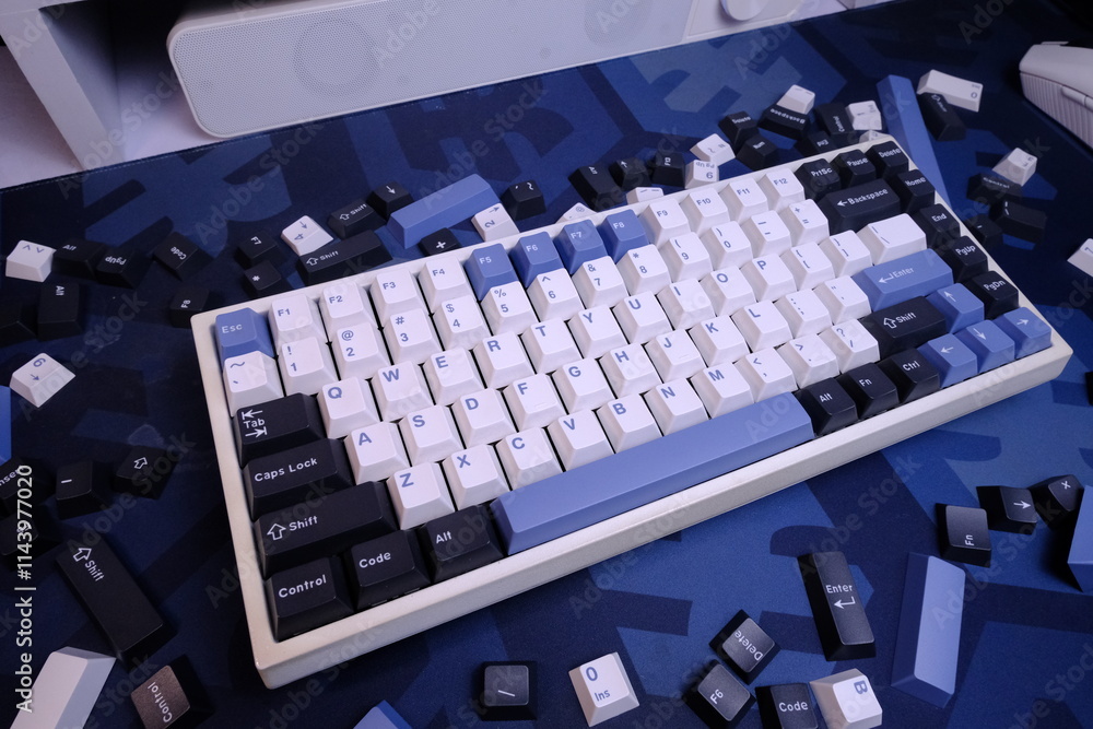 Fototapeta premium Modern 75% Layout White Mechanical Keyboard With Minimalist Theme of White, Blue, and Black Keycaps on a Blue Deskmat, with Scattered Keycaps