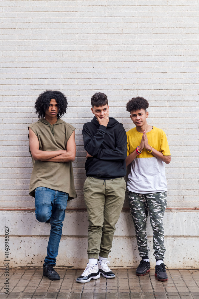 Obraz premium full body of multiethnic teenager friends with folded hands leaning against white brick wall, concept of friendship in youth and urban lifestyle, copyspace for text