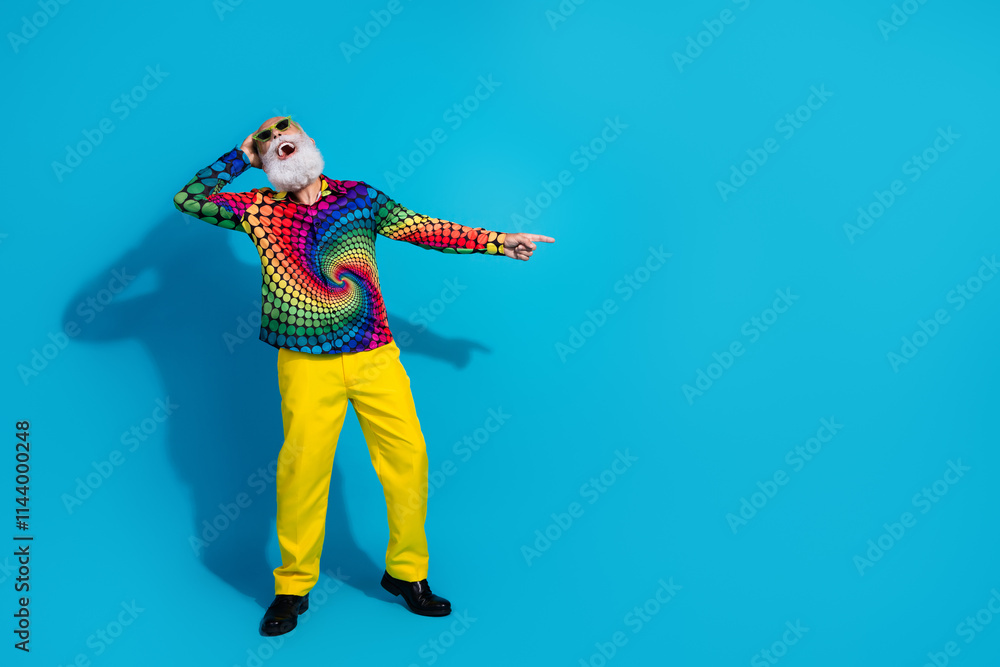 Full length photo of eccentric funky aged man laugh point finger empty space isolated on blue color background Full length photo of eccentric funky aged man laugh point finger empty space isolated on blue color background