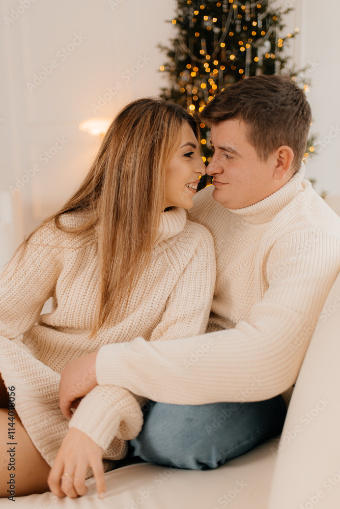Young happy couple embracing and relaxing on comfortable couch. Lovely couple sitting on sofa wearing christmas sweater and hugging. Young happy couple embracing and relaxing on comfortable couch. Lovely couple sitting on sofa wearing christmas sweater and hugging.