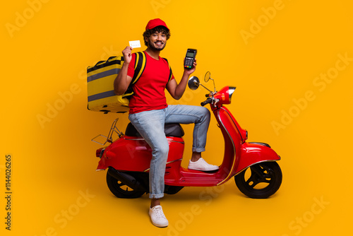 Young smiling delivery courier on red scooter holding card against bright yellow background photo