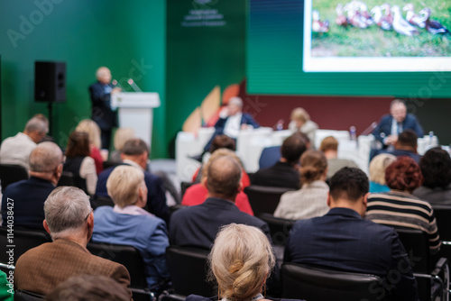 Room filled with attentive audience listening to speakers on stage during conference panel discussion.