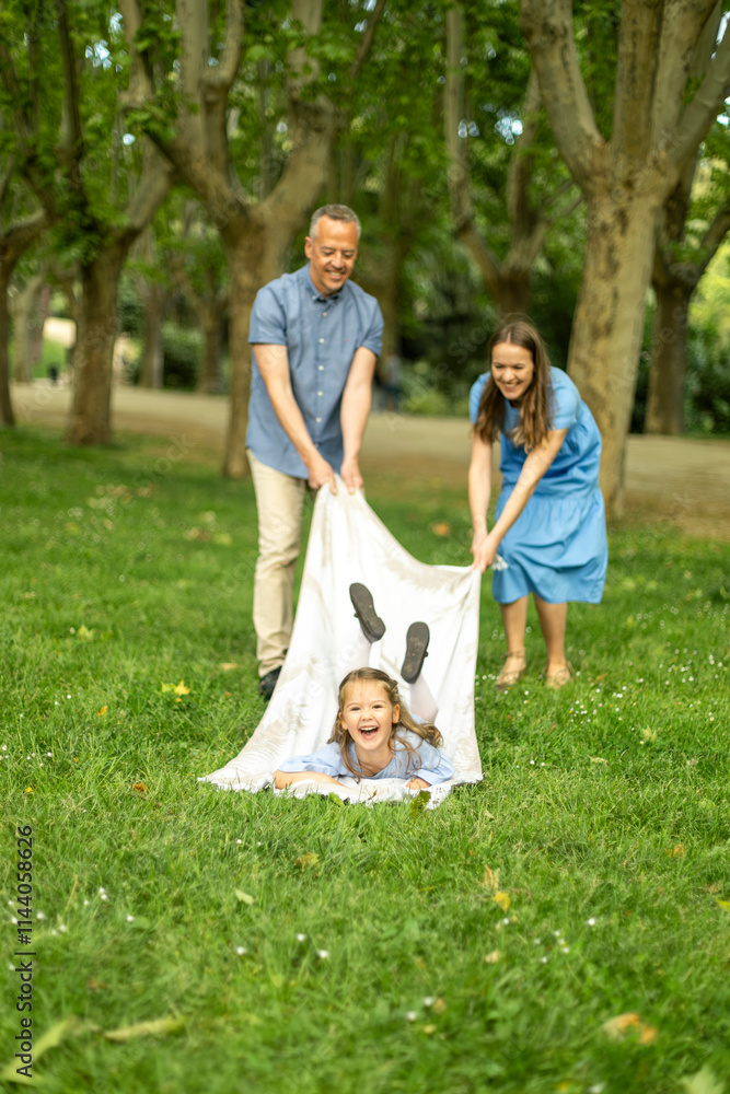 Parents playing with their daughter rolling her into a blanket in a park Parents playing with their daughter rolling her into a blanket in a park