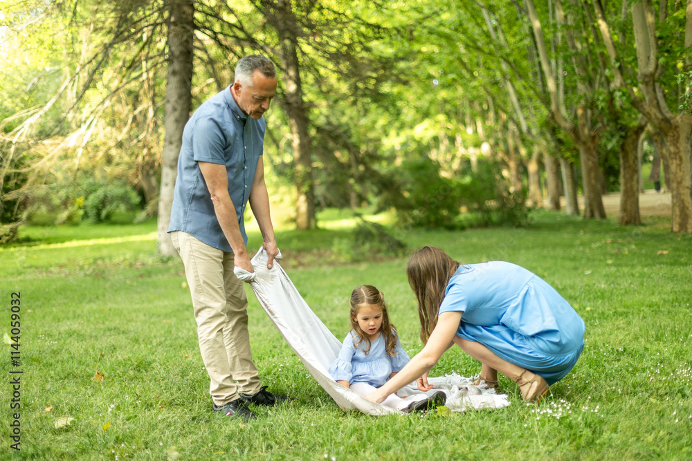 Parents wrapping daughter in blanket in park during summer day Parents wrapping daughter in blanket in park during summer day
