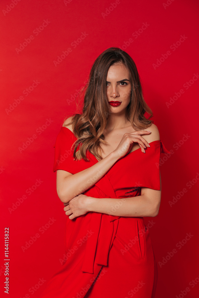 Adorable slender woman in a fashionable red dress. Woman posing on a red background. Advertising of fashionable womens clothing.