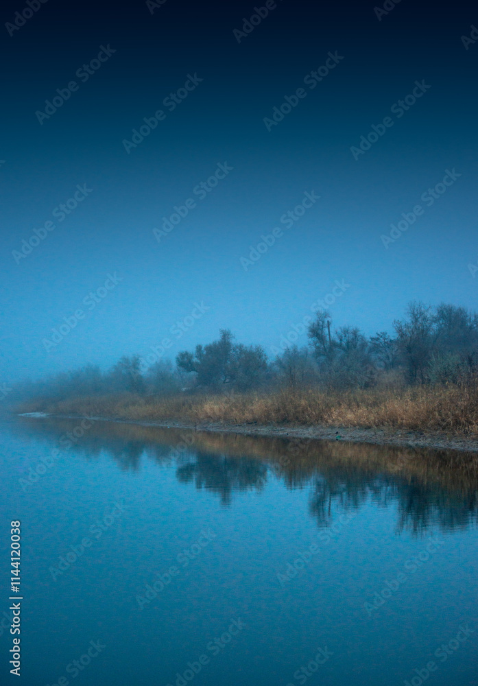 Fototapeta premium Autumn morning on the blu lake with fog , reflections on water ,landscape photography .Blue colors ,blue water ,mystery weather on the ponf.Forest near the pond , morning landscape at autumn season