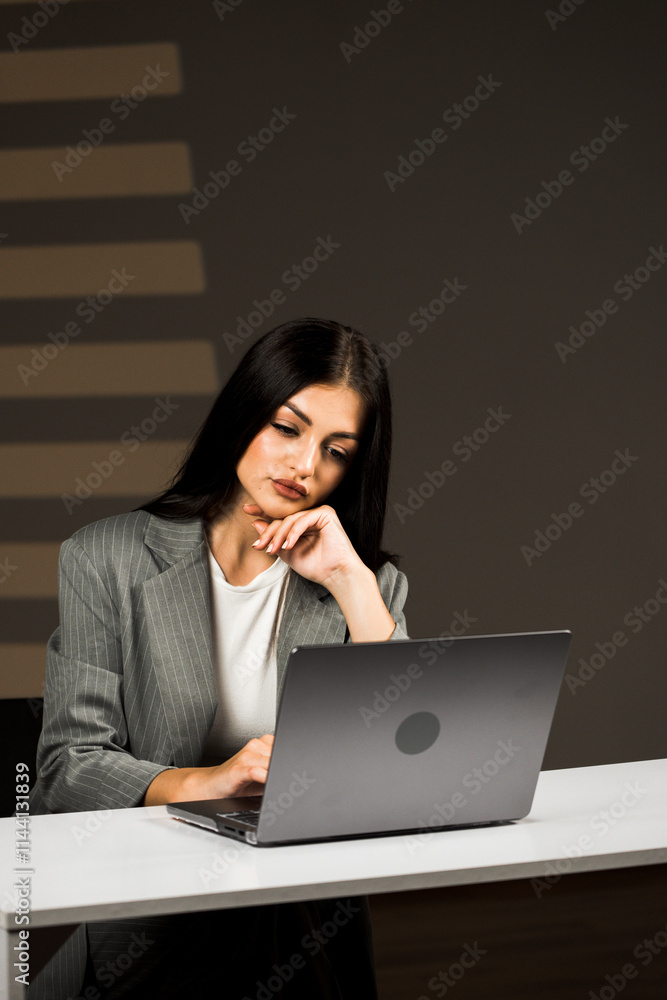 Young Business Woman Focused on Her Laptop in a Modern Office Environment, Demonstrating Remote Work Success and Professionalism in Her Attire Young Business Woman Focused on Her Laptop in a Modern Office Environment, Demonstrating Remote Work Success and Professionalism in Her Attire