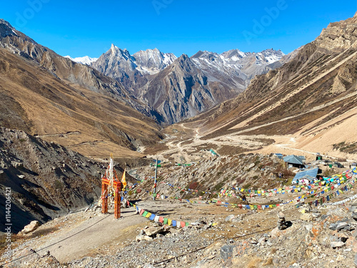 Sacred gate with flags and temple bell on the road leading to Om Parvat. Sheshnag Parvat, a snake-shaped mountain, in the background photo