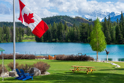 Fototapeta Naklejka Na Ścianę i Meble -  Canadian flag and mountains and trees. Jasper National Park summer landscape. Lac Beauvert Trail (Beauvert Lake).