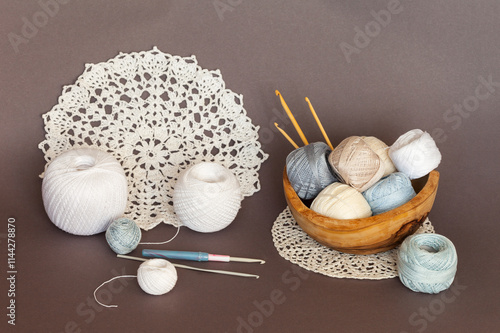 Close-up of wooden bowl with skeins of light natural cotton yarn for crocheting, crochet hooks and handmade lace round doilies on brown background. Crochet as hobby. DIY concept. Beautiful still life