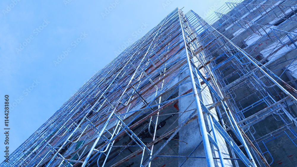 Scaffolding next to a new building. Building under construction with metal scaffolding set beside a commercial or residential building on a crane and sky background with copy space and selective focus Scaffolding next to a new building. Building under construction with metal scaffolding set beside a commercial or residential building on a crane and sky background with copy space and selective focus