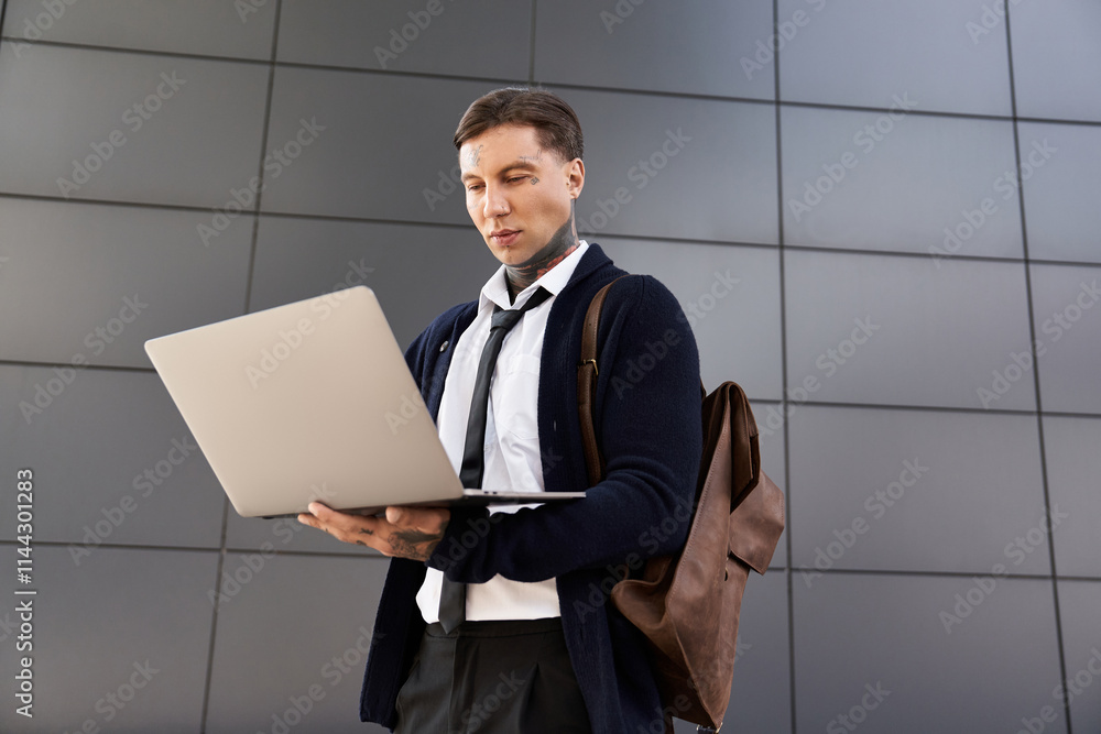 Handsome man with tattoos is focused on his laptop while standing in a contemporary setting. Handsome man with tattoos is focused on his laptop while standing in a contemporary setting.