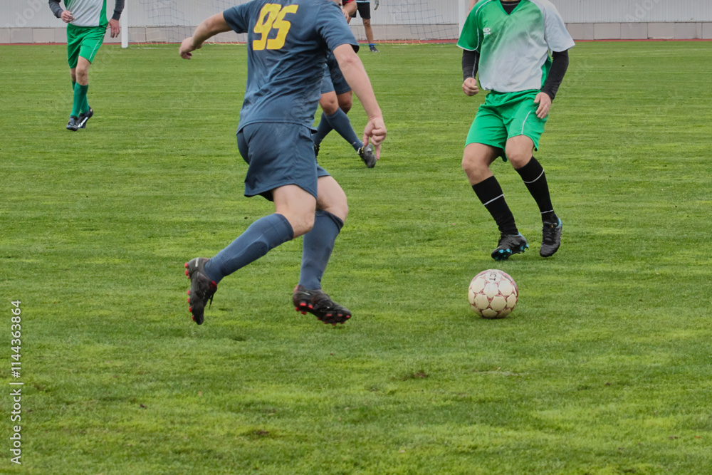 attacking soccer player in a blue uniform is preparing to pass the ball forward, game tactics in football, footballer with the ball on the green football field close-up. attacking soccer player in a blue uniform is preparing to pass the ball forward, game tactics in football, footballer with the ball on the green football field close-up.