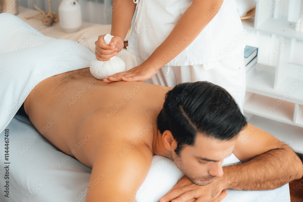 Hot herbal ball spa massage body treatment, masseur gently compresses herb bag on man body. Tranquil and serenity of aromatherapy recreation in day lighting ambient at spa salon. Quiescent Hot herbal ball spa massage body treatment, masseur gently compresses herb bag on man body. Tranquil and serenity of aromatherapy recreation in day lighting ambient at spa salon. Quiescent