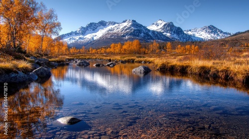 Snow-capped mountains rise above a calm river reflecting autumn trees and a clear blue sky.