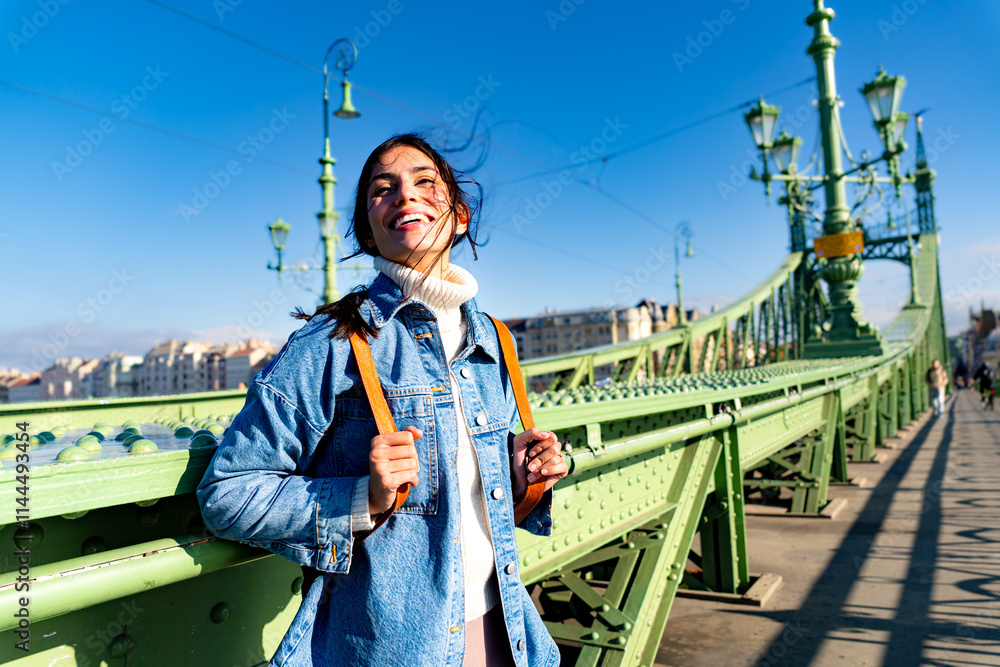 Fototapeta premium A smiling woman looking around joyfully, with her hair blowing in the wind, enjoying the moment on the bridge