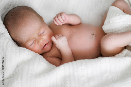 A baby is sleeping on a white blanket. The baby is small and has a hand on its face