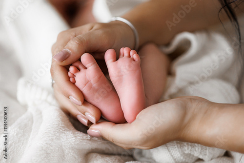A baby's feet are being held by a woman. The baby is small and has a pink color. The woman is holding the baby's feet gently, and the baby is resting comfortably in her arms. Concept of warmth