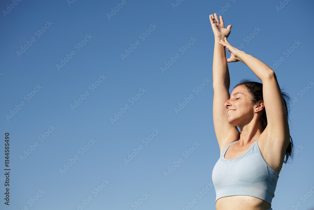 A smiling young woman practices yoga and stretching on a sunlit green meadow with a blue sky in the background. Concept of connecting with nature, benefits of practicing yoga, pilates, meditation. A smiling young woman practices yoga and stretching on a sunlit green meadow with a blue sky in the background. Concept of connecting with nature, benefits of practicing yoga, pilates, meditation.