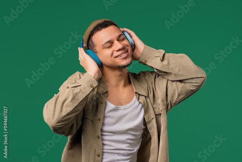 Hipster positive man listening music, enjoying with headphones, green studio photo