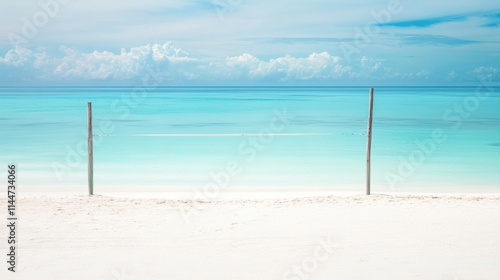 Pristine white sandy beach with two wooden poles framing a tranquil turquoise ocean under a vibrant blue sky, featuring soft clouds and a serene tropical atmosphere.