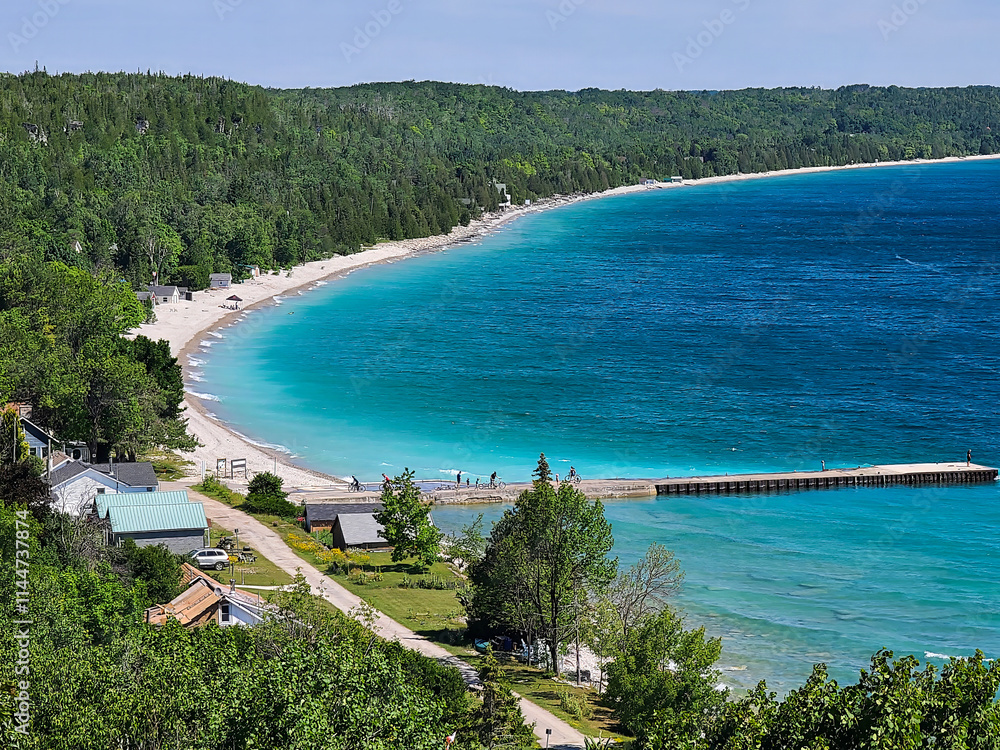 Naklejka premium Looking down on the deep blue and turquoise waters and dock of a bay, surrounded by lush green forests, on a sunny day.
