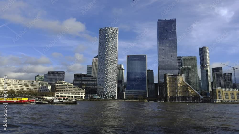The video captures Canary Wharf's skyline with One Canada Square, a yellow and red ferry on the Thames, and a clear blue sky in London. The video captures Canary Wharf's skyline with One Canada Square, a yellow and red ferry on the Thames, and a clear blue sky in London.