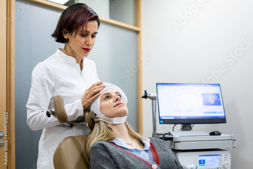 An adult female psychiatrist is placing a transcranial magnetic stimulation device on a young girl to treat mental illness in a medical clinic. TMS concept.